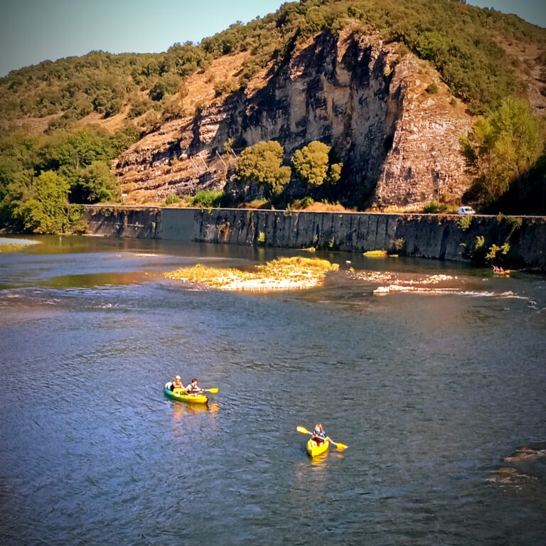 2 canoë solos jaunes et verts et 1 canoe duo sur la rivière Ardèche sous le pont de sampzon des pagaies doubles jaunes, on aperçoit la route qui longe la rivière Ardèche au niveau du pont de Sampzonavec